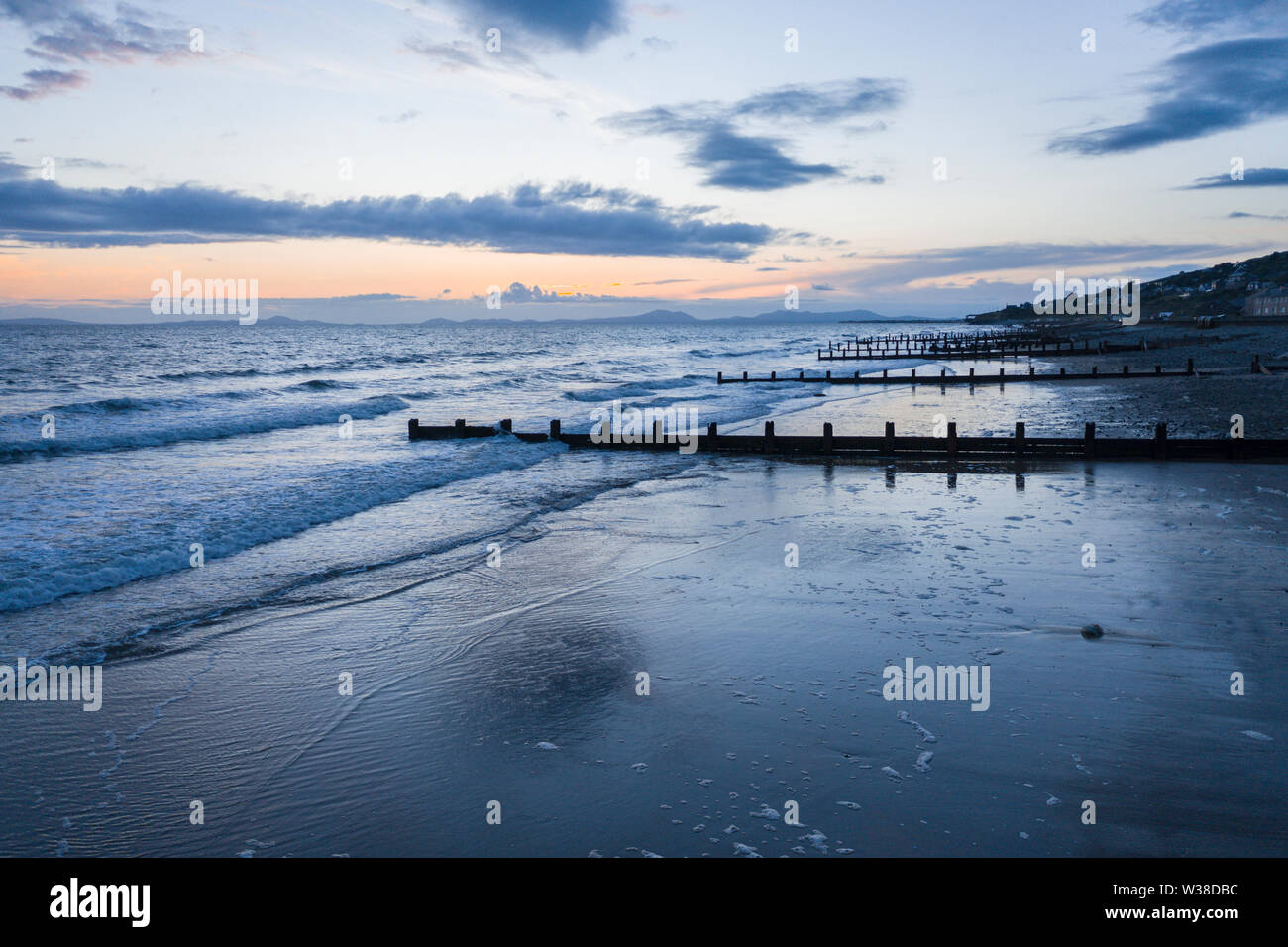 Nuvole temporalesche al crepuscolo sulla spiaggia panoramica con waterbreak in legno. Blaenau Ffestiniog in Galles, Regno Unito Foto Stock