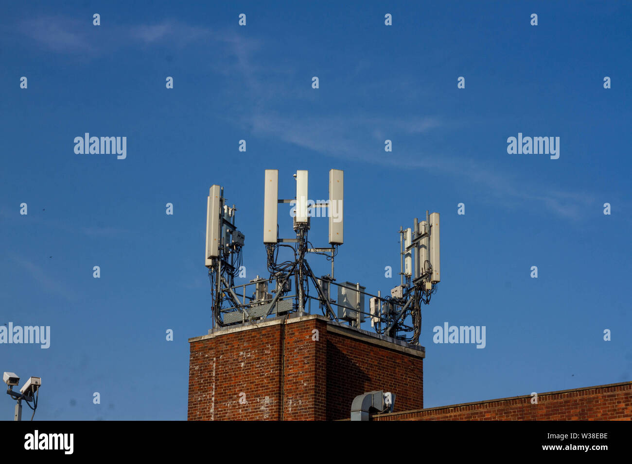 WIfi o telefono cellulare antenna visto sulla parte superiore di un nuovo edificio in mattoni di fronte blu cielo Foto Stock