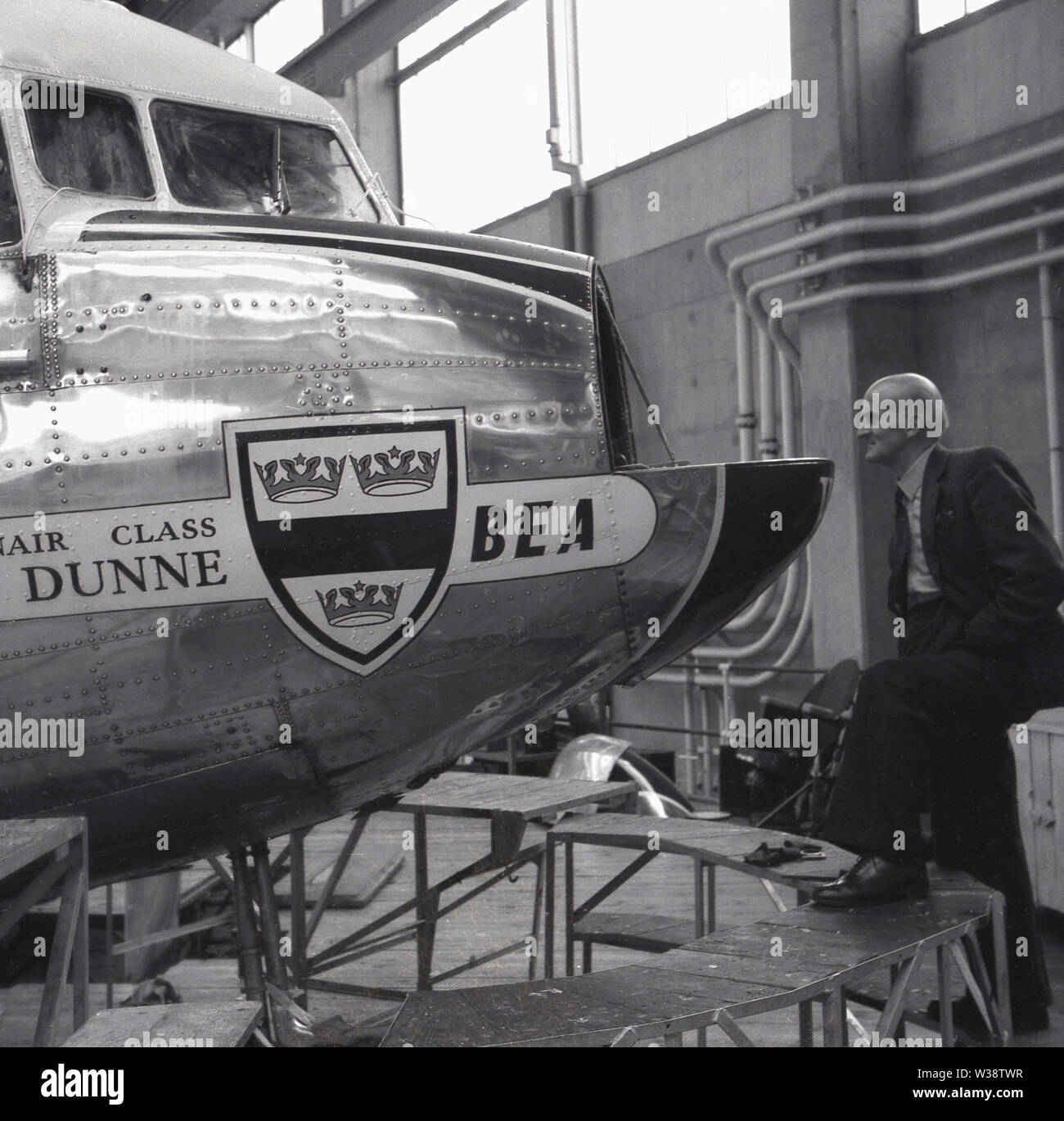 Anni sessanta, storico, uomo in appendiabiti guardando il stainlees acciaio parte anteriore o naso di un aeromobile BEA, Dunne, un Douglas DC-3, Inghilterra, Regno Unito. Foto Stock