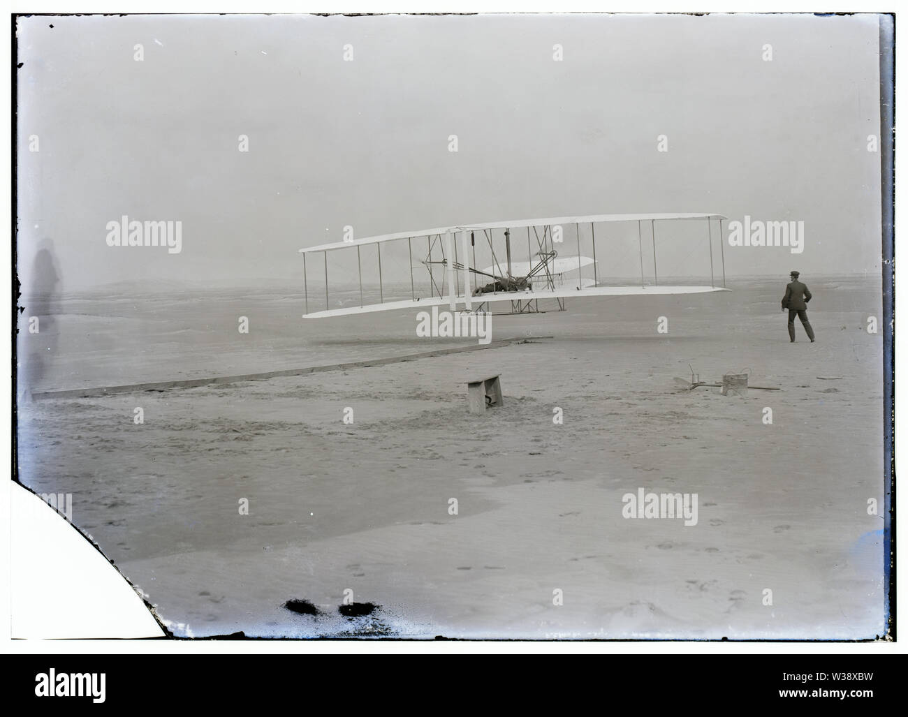 Primo volo, 120 metri in 12 secondi, 10:35 del mattino; Kitty Hawk, North Carolina; altri primo volo, Dicembre 17, 1903; Riepilogo: fotografia mostra il primo powered, controllata, un volo prolungato. Orville Wright ai comandi della macchina, che giace prono sulla aletta inferiore con fianchi in culla che gestiva l'ala-meccanismo di orditura. Wilbur Wright che costeggia per bilanciare la macchina, ha appena rilasciato la sua presa sul montante in avanti del parafango destro. La rampa di partenza, l'ala-resto, una bobina box, e gli altri elementi necessari per la preparazione del volo sono visibili dietro la macchina. (Orville Wright Foto Stock
