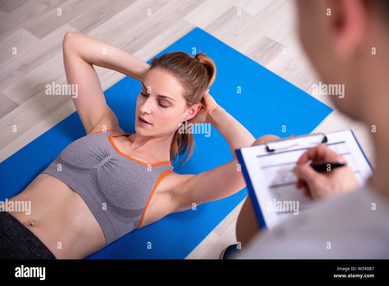 Sporty giovane donna facendo sit ups su materassino yoga accanto al Trainer Holding negli appunti Foto Stock