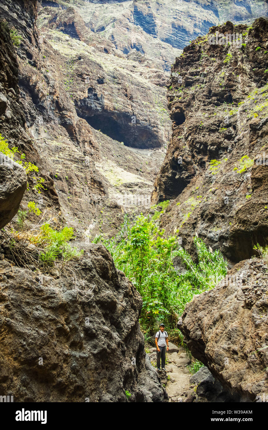 Giovani traveler rimane sulla sommità di un enorme masso in Masca gorge, Tenerife, mostrando solidificato di lava vulcanica di strati di flusso e la formazione di arco. Burrone Foto Stock