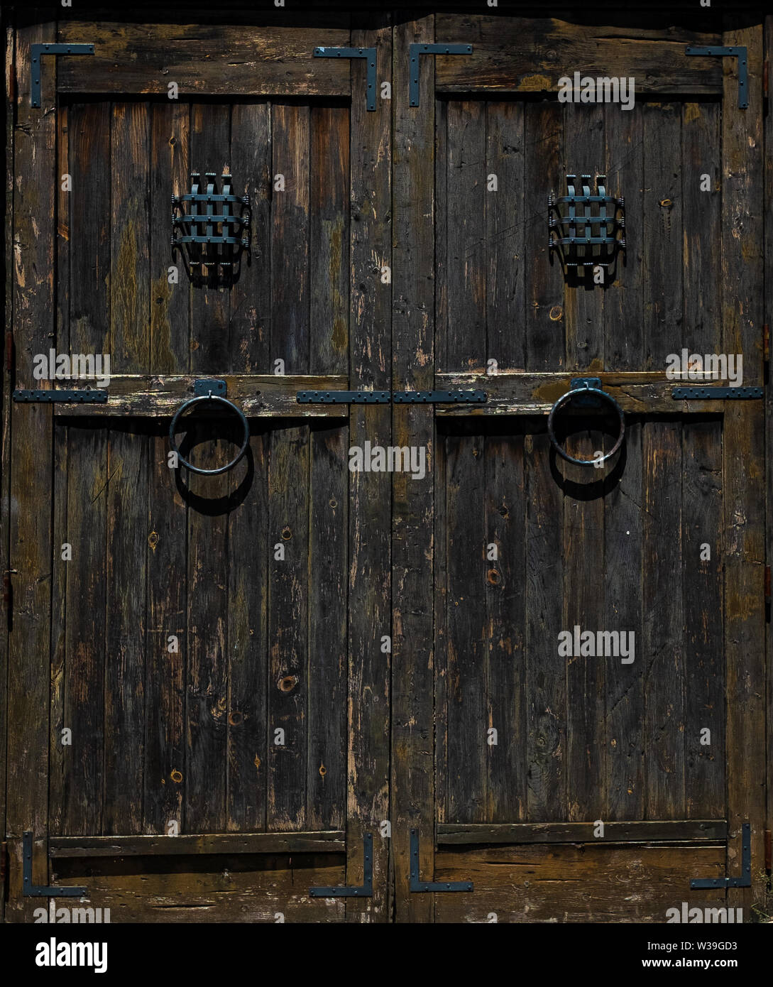 Primo piano di una doppia porta in legno intemprata con maniglie ad anello in metallo e piccole finestre barrate in uno stile rustico e antico Foto Stock