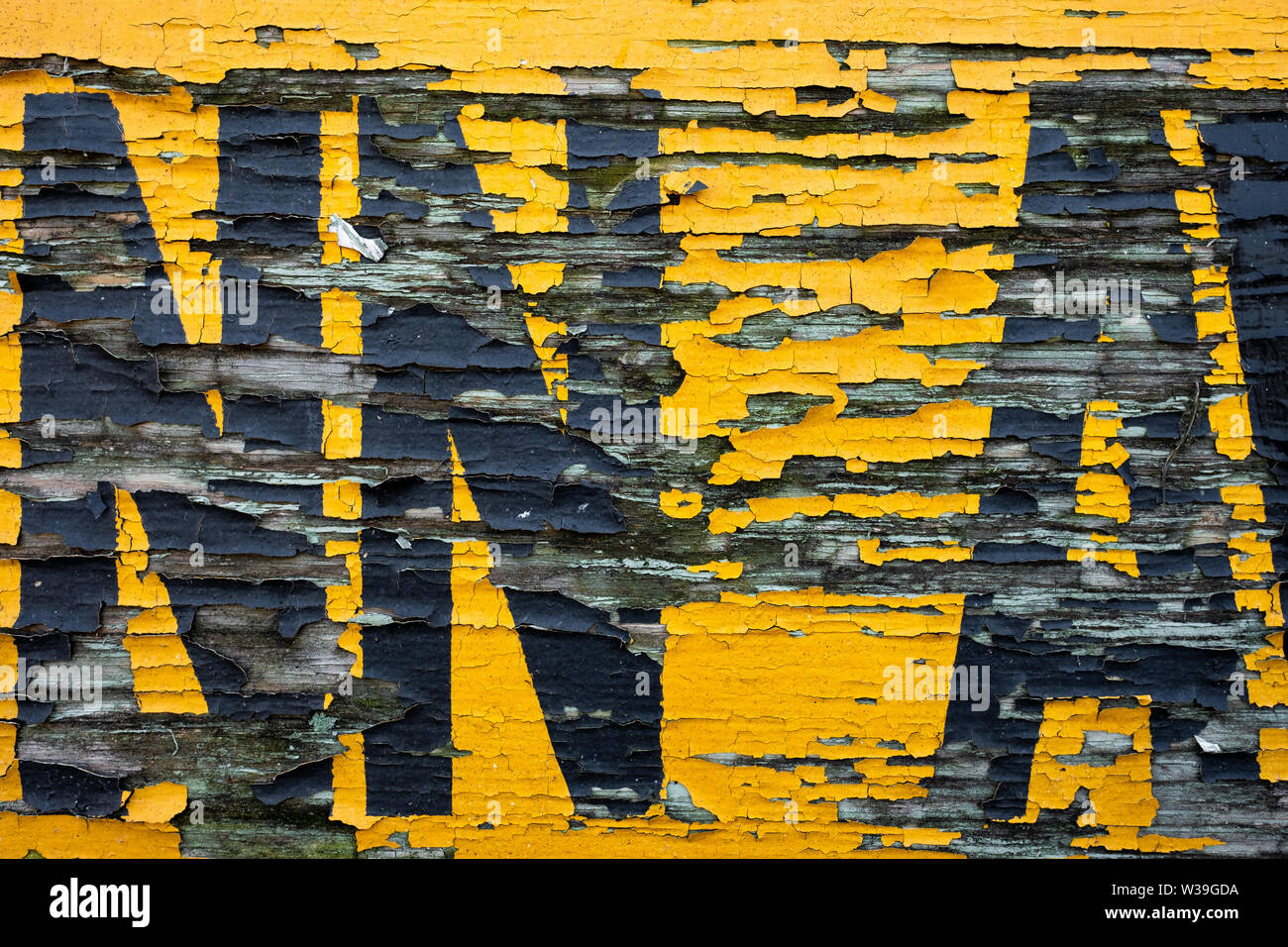 Primo piano di una superficie verniciata con agenti atmosferici e sbucciati con lettere gialle e nere sbiadite su sfondo in legno deteriorato Foto Stock