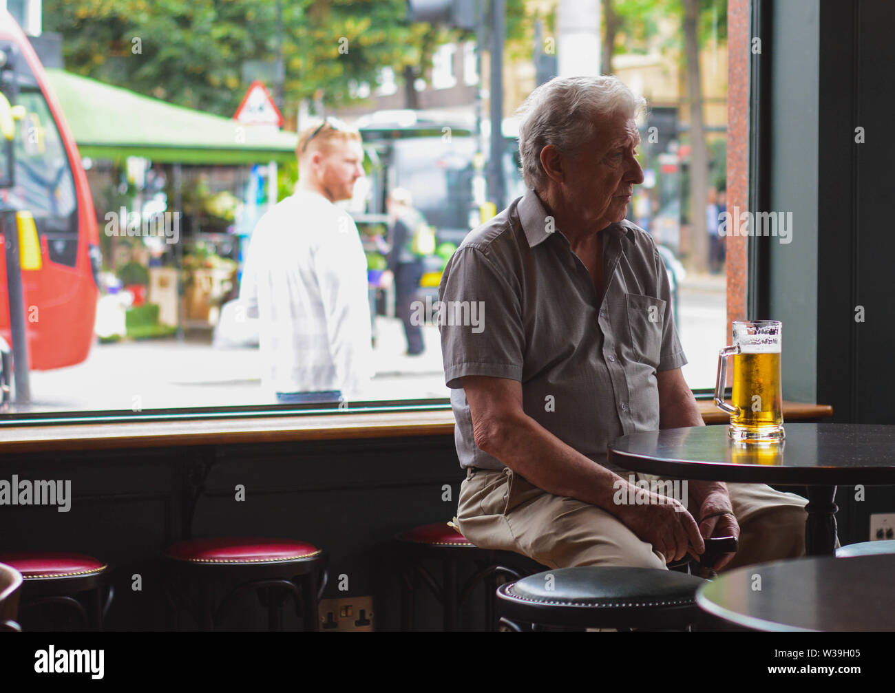 Il vecchio uomo avente un drink da sola in un pub Foto Stock