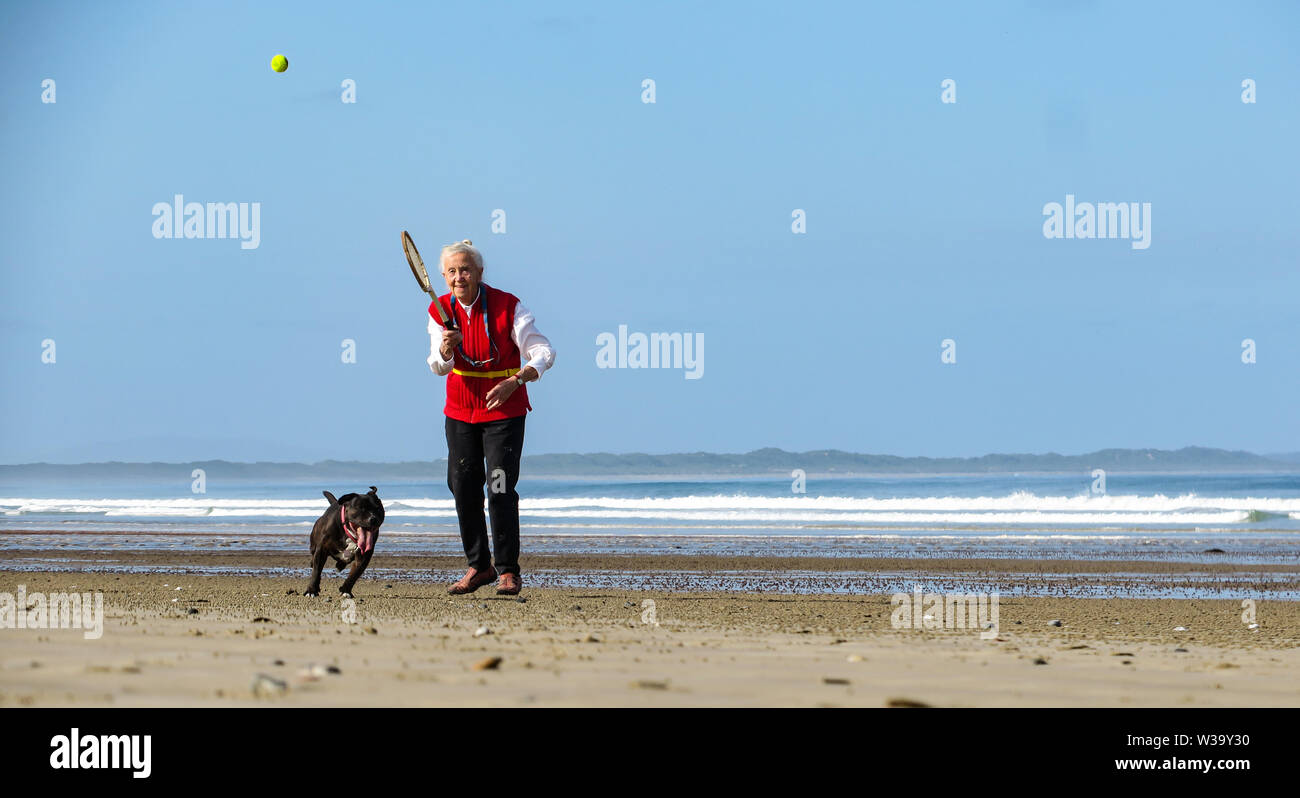 Una vecchia signora ha colpito la palla da tennis al suo cane sulla spiaggia. Foto Stock