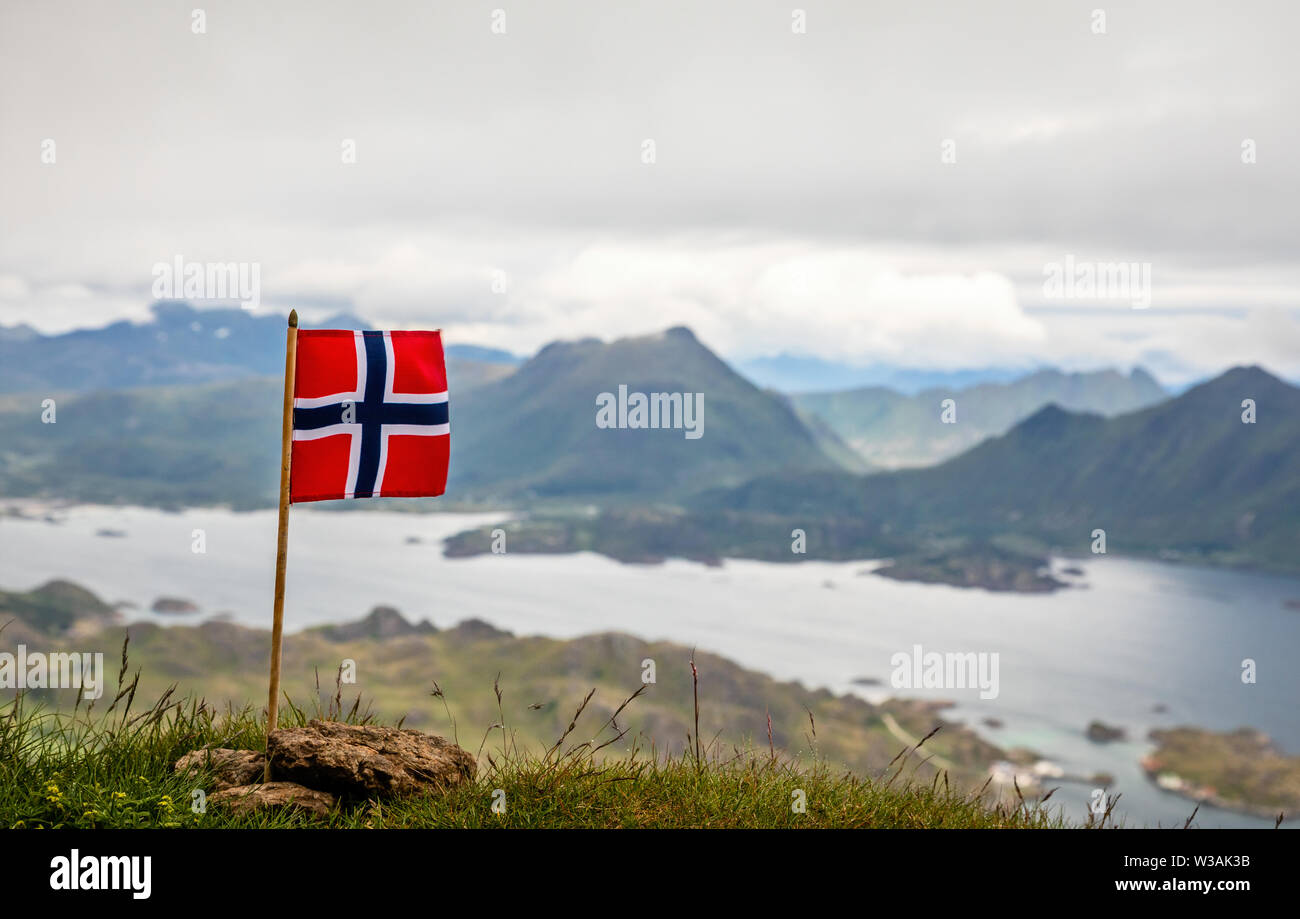 Norwegian bandiera nazionale nel vento sulla sommità del picco Nonstinden con fjord in background, Ballstad, Vestvagoy comune, Nordland county, né Foto Stock