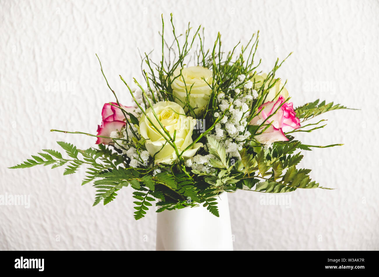 Close-up ancora vita di un fiore disposizione con le rose in un vaso bianco contro parete bianca, all'interno, soggiorno Foto Stock