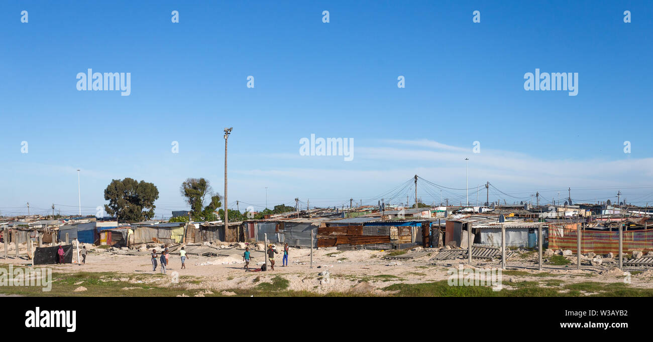 Gruppo di poveri neri africani i bambini che giocano a calcio o di calcio al di fuori di una capanna di stagno insediamento informale o squatter camp in Cape Town, Sud Africa Foto Stock