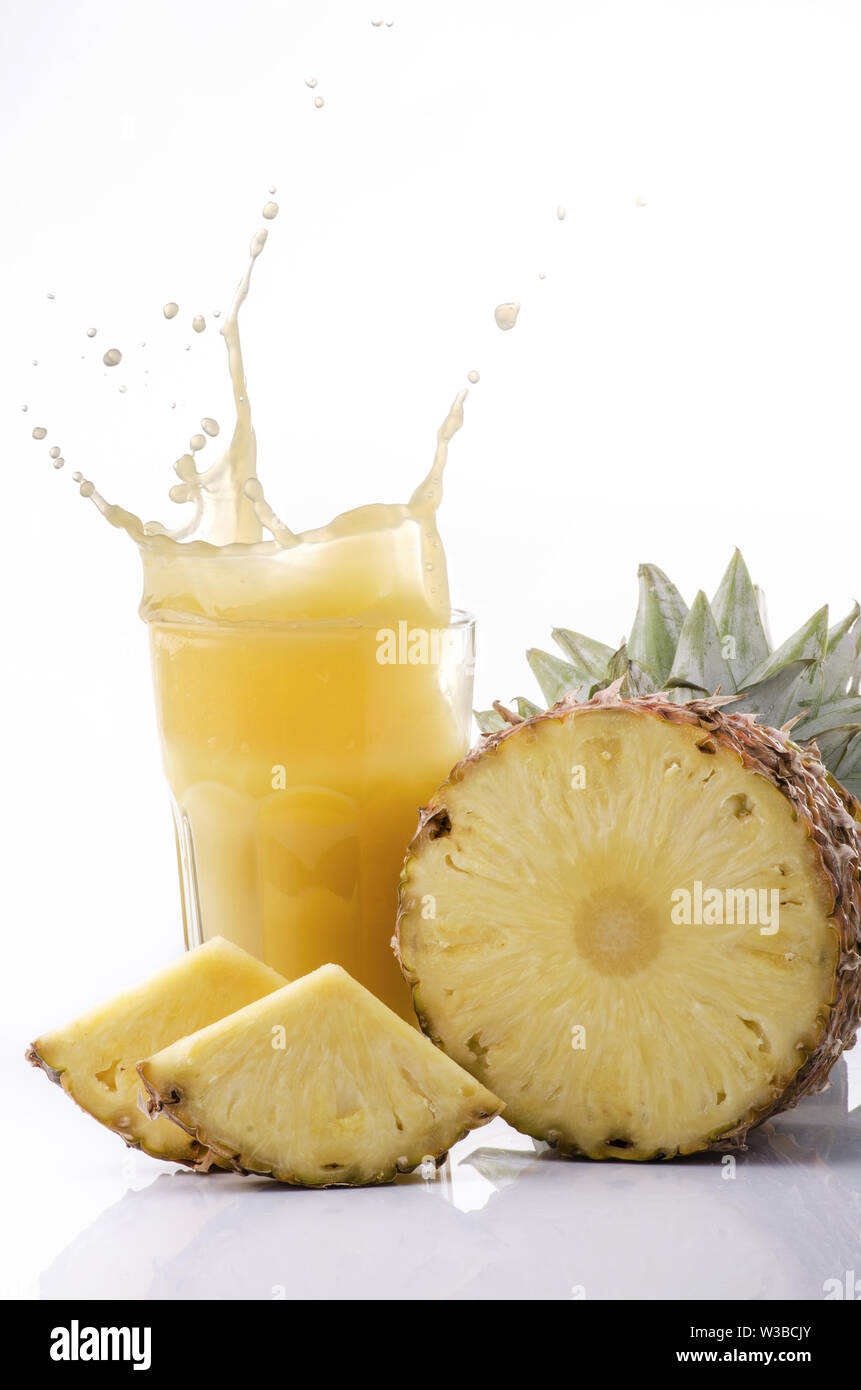 Ananas tagliato a fettine e succo di colore giallo che esplode da un vetro isolato su sfondo bianco Foto Stock