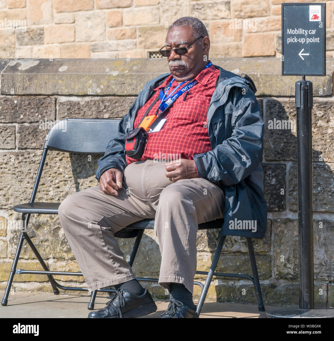 Un anziano uomo nero, sonnecchia seduto in una sedia, nel caldo sole primaverile sul Castello di Edimburgo promenade. La Scozia, Regno Unito. Foto Stock