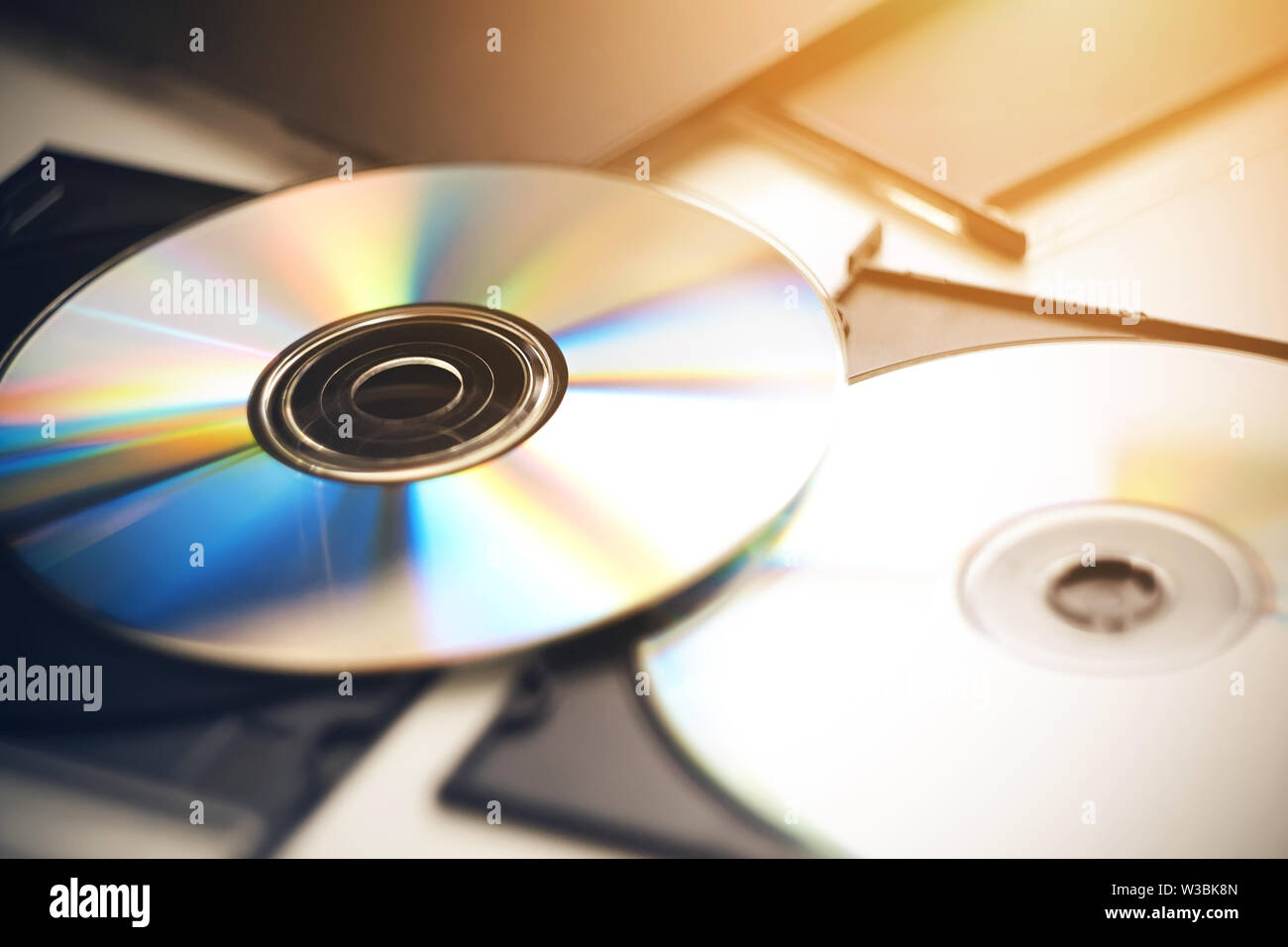 Diversi cd giacciono su un tavolo bianco nelle loro scatole nere, illuminato dalla luce solare e scintillante con colori diversi. Foto Stock