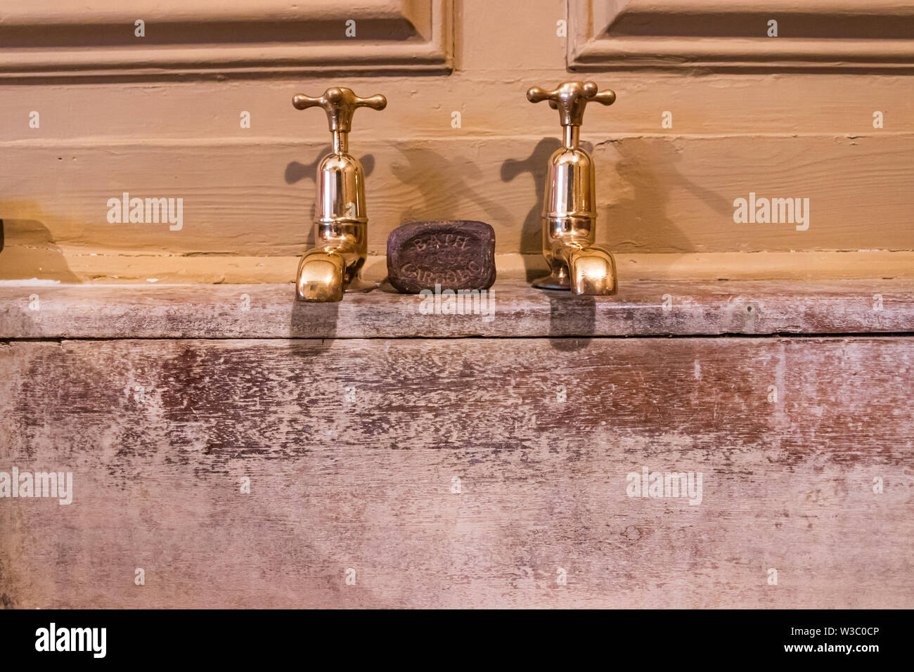 Un vecchio bar di sapone fenico tra due antichi rubinetti in ottone al di sopra di un vecchio legno bianco area di lavaggio Foto Stock