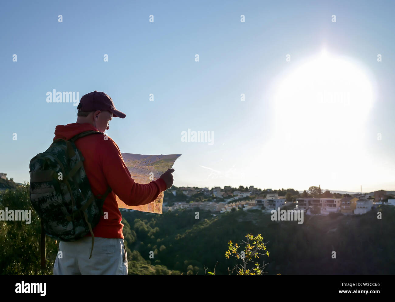 Tourist guy esamina una mappa, si erge sullo sfondo della città su una collina Foto Stock