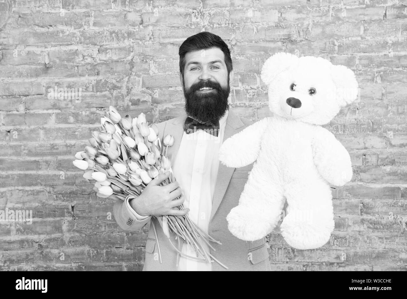 Macho getting ready data romantico. In attesa di Darling. L'uomo ben curato usura tuxedo bow tie tenere fiori tulipani bouquet e grande orsacchiotto giocattolo. Invitatela dating. Regalo romantico. Uomo romantico. Foto Stock