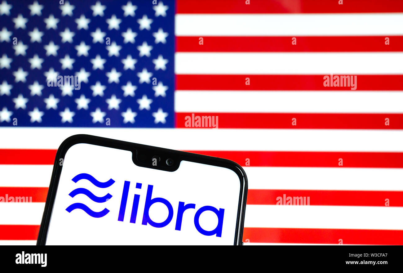 Facebook Libra crypto logo valuta sullo smartphone e sfocata bandiera degli stati uniti in corrispondenza di uno schermo portatile sullo sfondo. Foto concettuale. Foto Stock