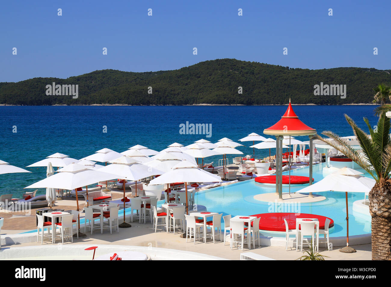 Bella estate panoramico con vista della spiaggia, il bianco e il rosso ombrelloni vicino alla piscina di lusso. Moda bianco sdraio sulla spiaggia in riva al mare Foto Stock
