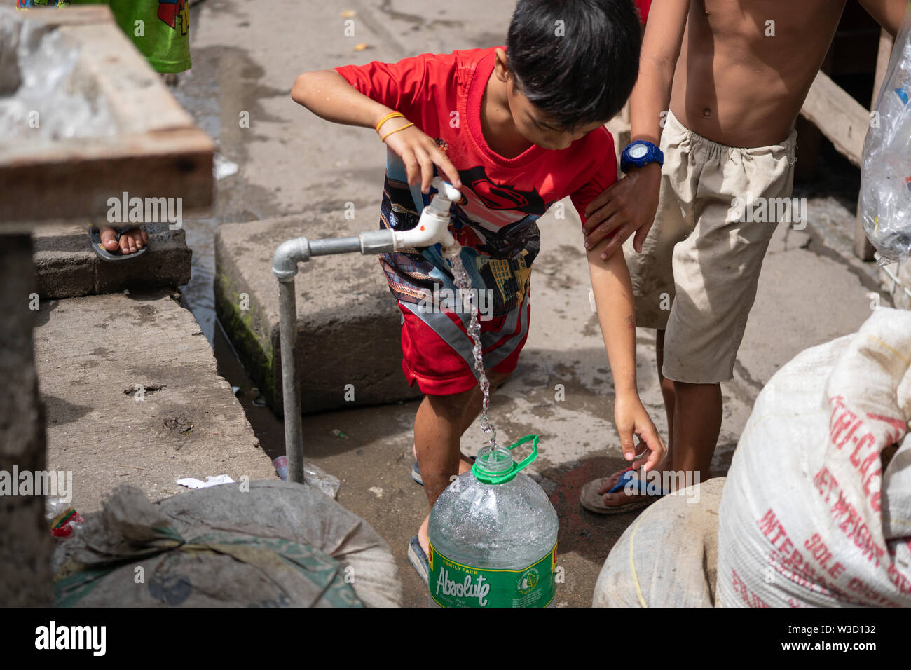 Un giovane ragazzo di riempimento in plastica di un contenitore di acqua da un permanente della tubazione dell'acqua all'interno di una comunità povera,Cebu, Filippine. Foto Stock