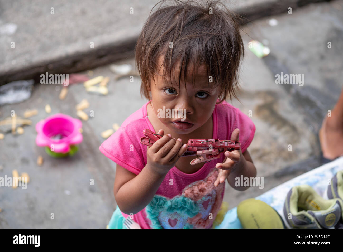 Una giovane ragazza filippina in una comunità povera giocando con un numero di pioli di plastica cercando fino alla fotocamera,Cebu, Filippine. Foto Stock