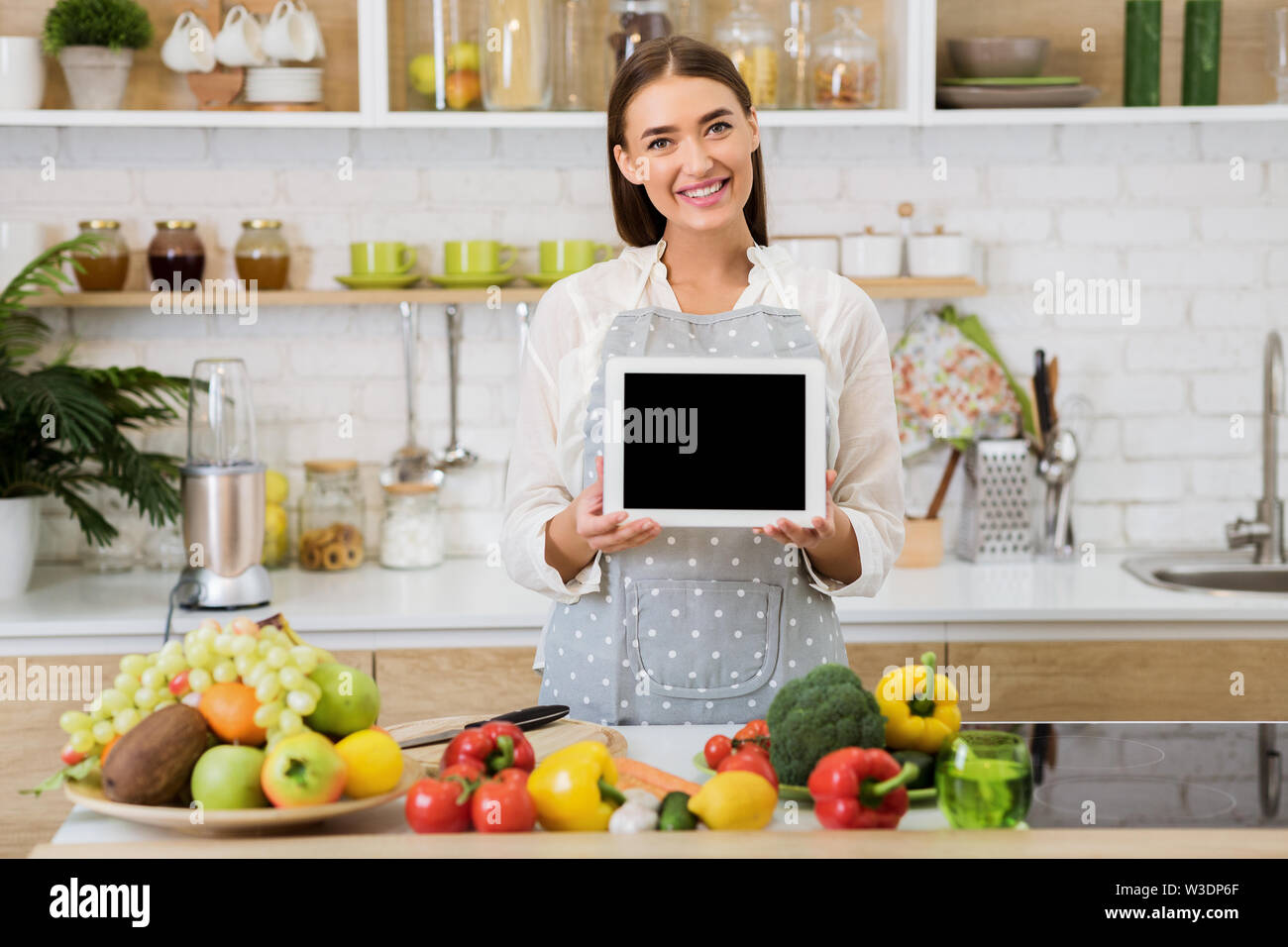 Donna che mantiene tablet con schermo vuoto, cena di cucina Foto Stock