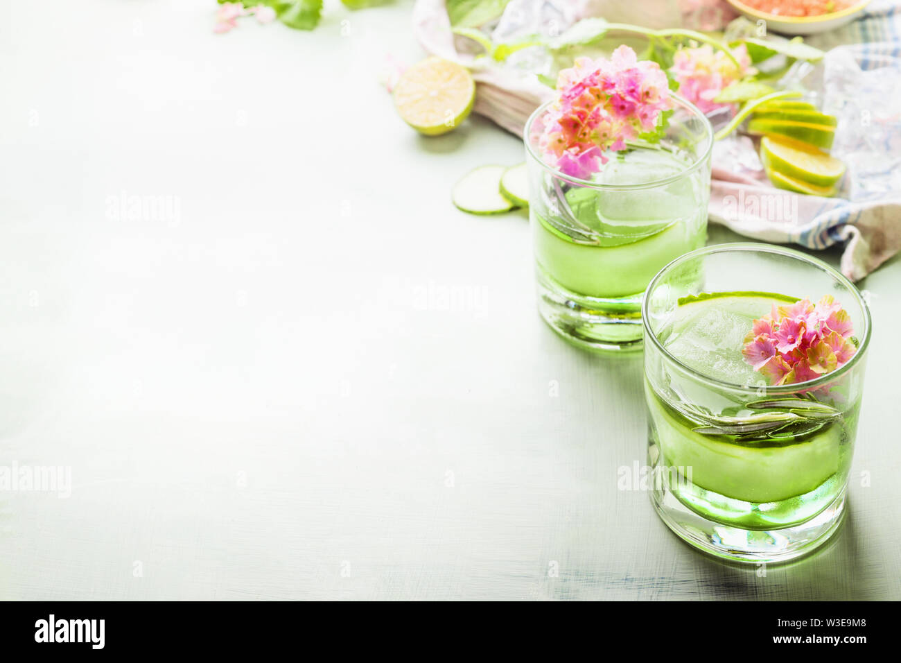 Verde estate rinfrescanti bevande con ghiaccio in bicchieri sul tavolo luminoso con ingredienti e fiori. Fresca limonata ghiacciata con il cetriolo e erbe aromatiche. Copia spa Foto Stock