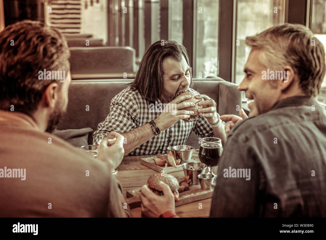 Fame longhaired uomo mangiare hamburger con piacere Foto Stock