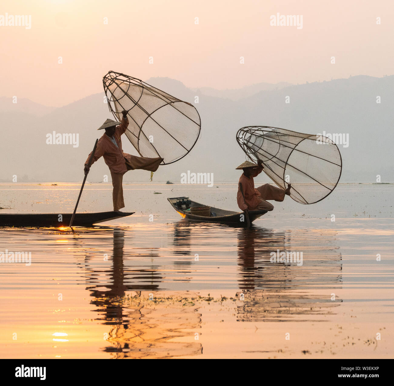 Inle, Myanmar - Marzo 2019: due tradizionale birmana gamba pescatori di canottaggio a Lago Inle durante il sunrise reti di contenimento in mani. Silhouette di retroilluminazione refle Foto Stock