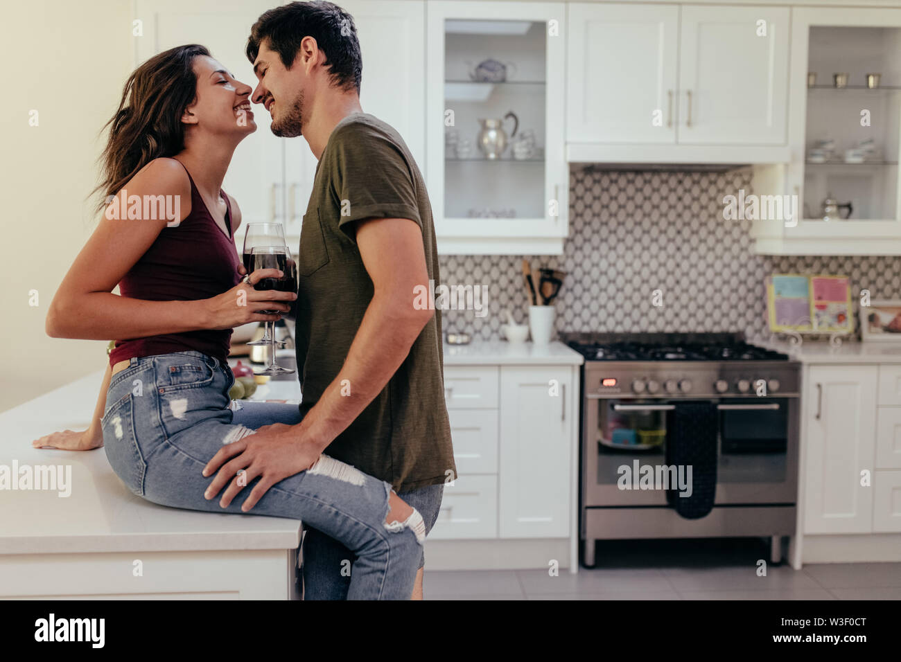 Giovane uomo e donna in amore con bicchieri di vino insieme nella cucina di casa. Coppia giovane romancing in cucina. Foto Stock