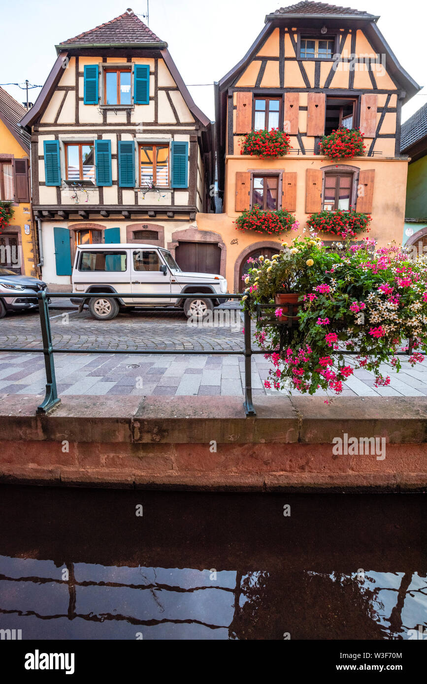 Fiore decorate brook e vecchie case con travi di legno con intaglio, villaggio Ribeauvillé, Alsazia, Francia, ubicazione della Strada del Vino Foto Stock