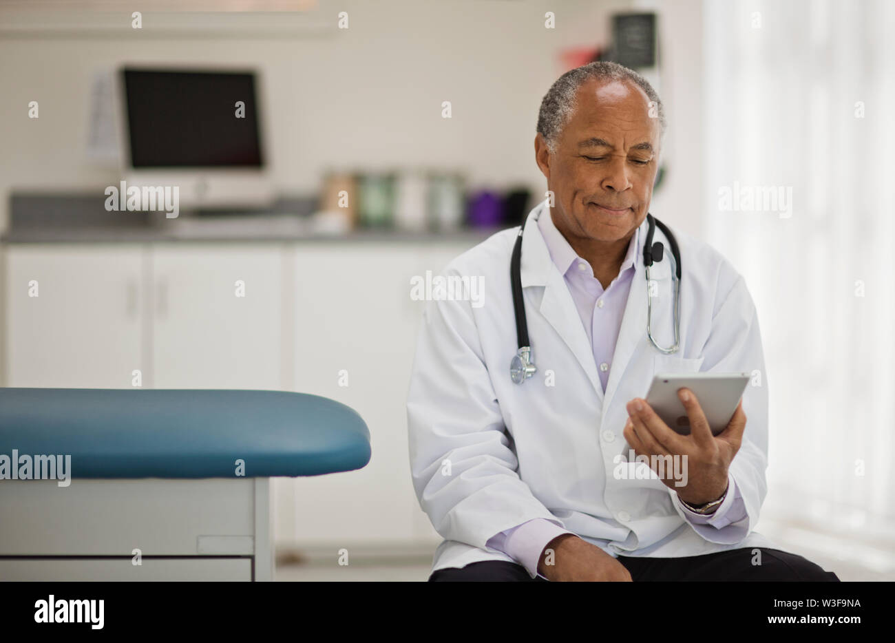 Contemplativa medico maschio utilizzando una tavoletta digitale mentre è seduto dentro il suo ufficio. Foto Stock