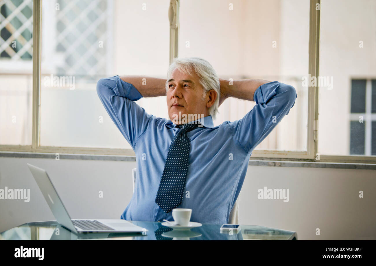 Imprenditore rilassato appoggia la schiena sulla sua sedia durante una pausa caffè presso la sua scrivania. Foto Stock
