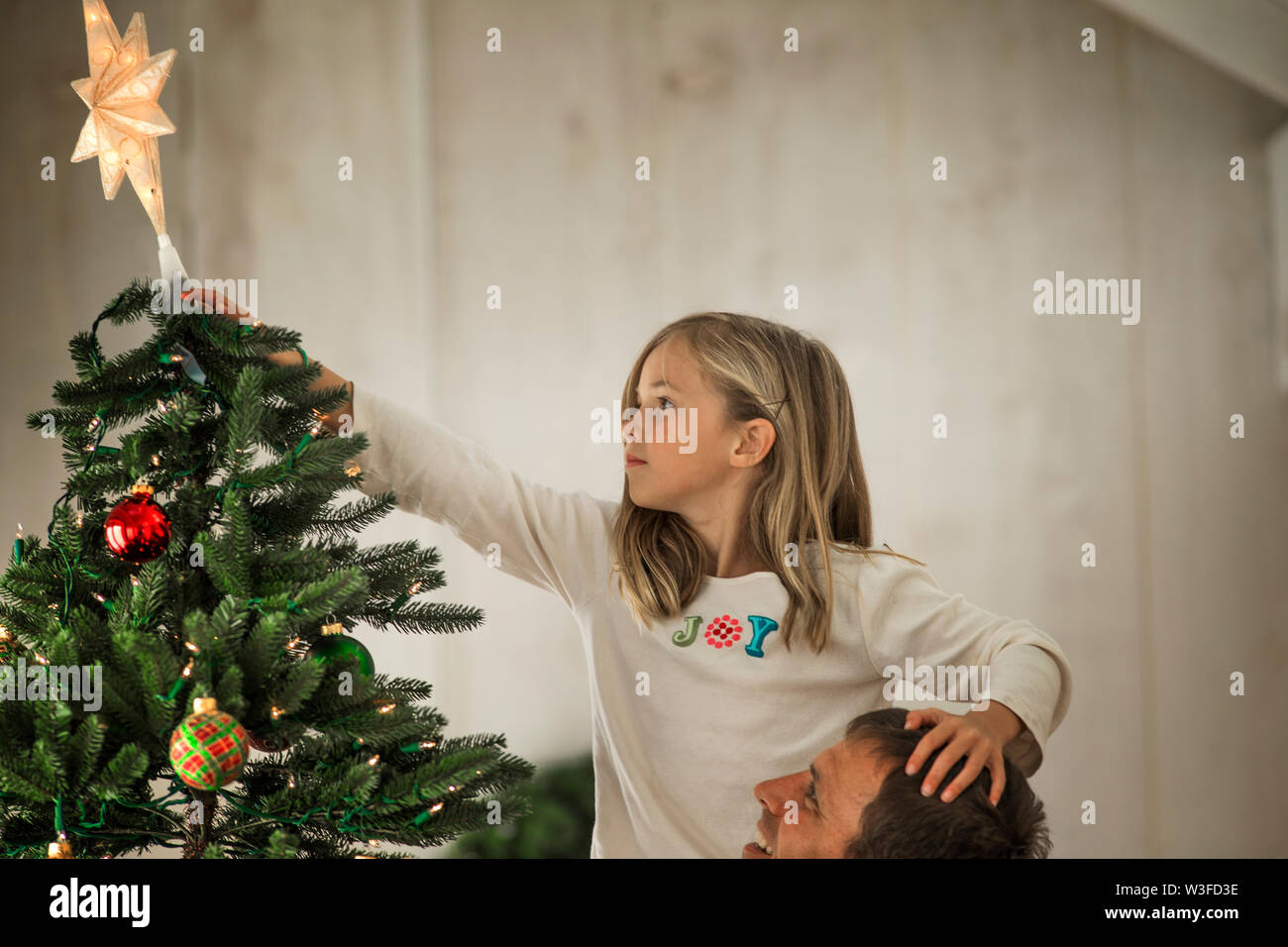 Ragazza giovane posizionando la stella sulla parte superiore dell'albero di Natale con suo padre. Foto Stock