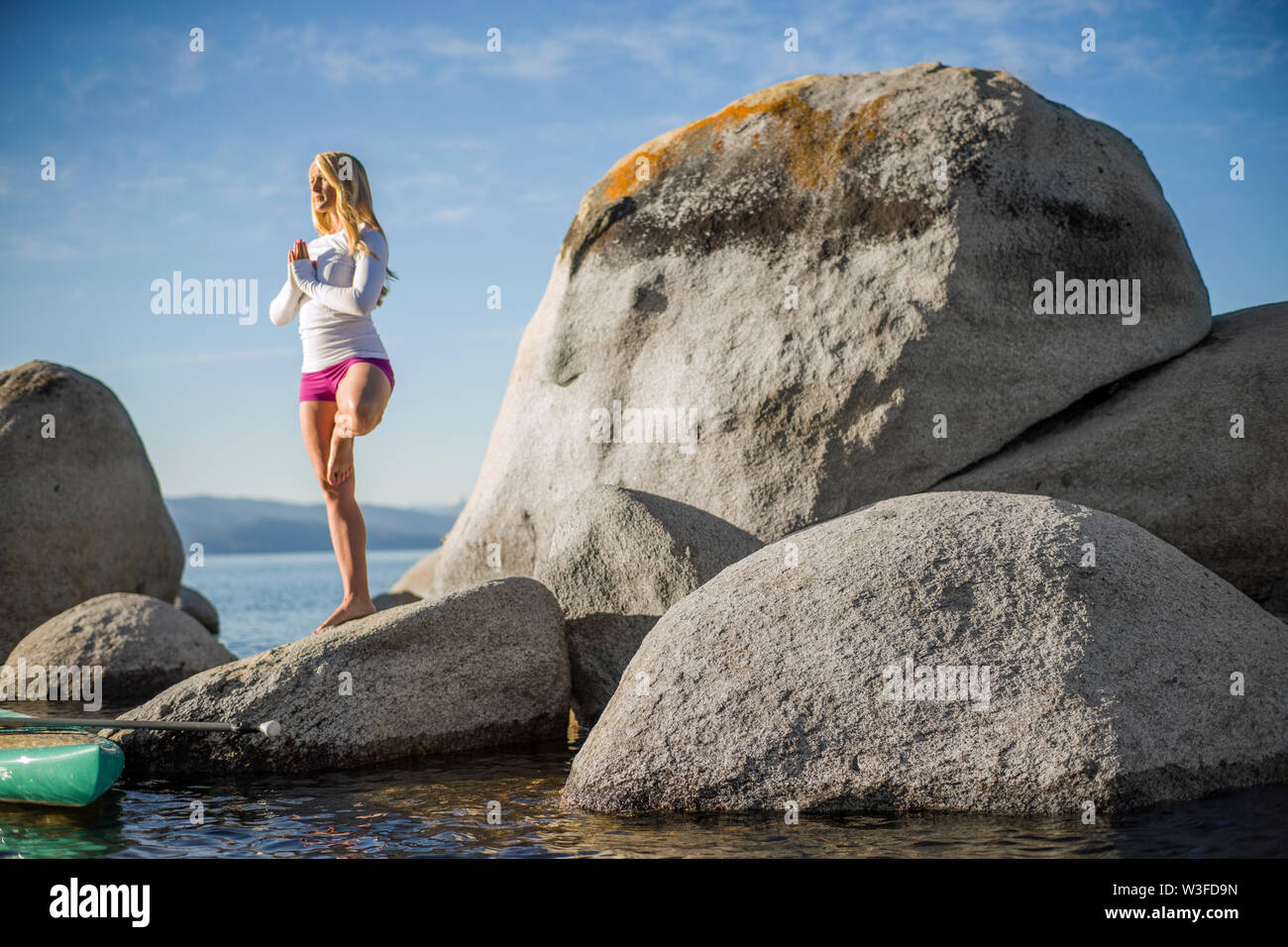 Attivo giovane donna a praticare yoga su rocce di grandi dimensioni vicino al mare. Foto Stock
