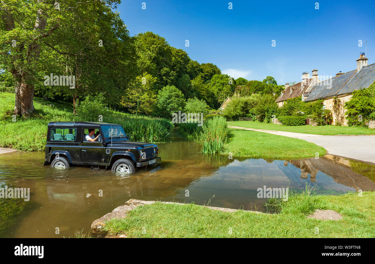 Land Rover Defender attraversando il fiume occhio ad un guado. Upper Slaughter, Cotswolds, Gloucestershire, Inghilterra, Regno Unito. Foto Stock