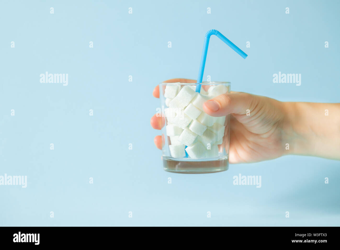 Eccessivo consumo di zucchero concetto - la mano che regge il vetro con cubetti di zucchero Foto Stock