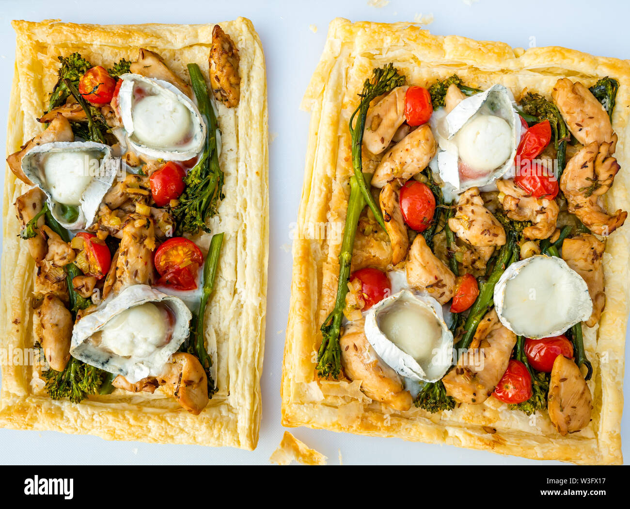 Estate cibo: pasto servito all'aperto con formaggio di capra, broccoli, pomodori e pollo su pasta sfoglia fette Foto Stock