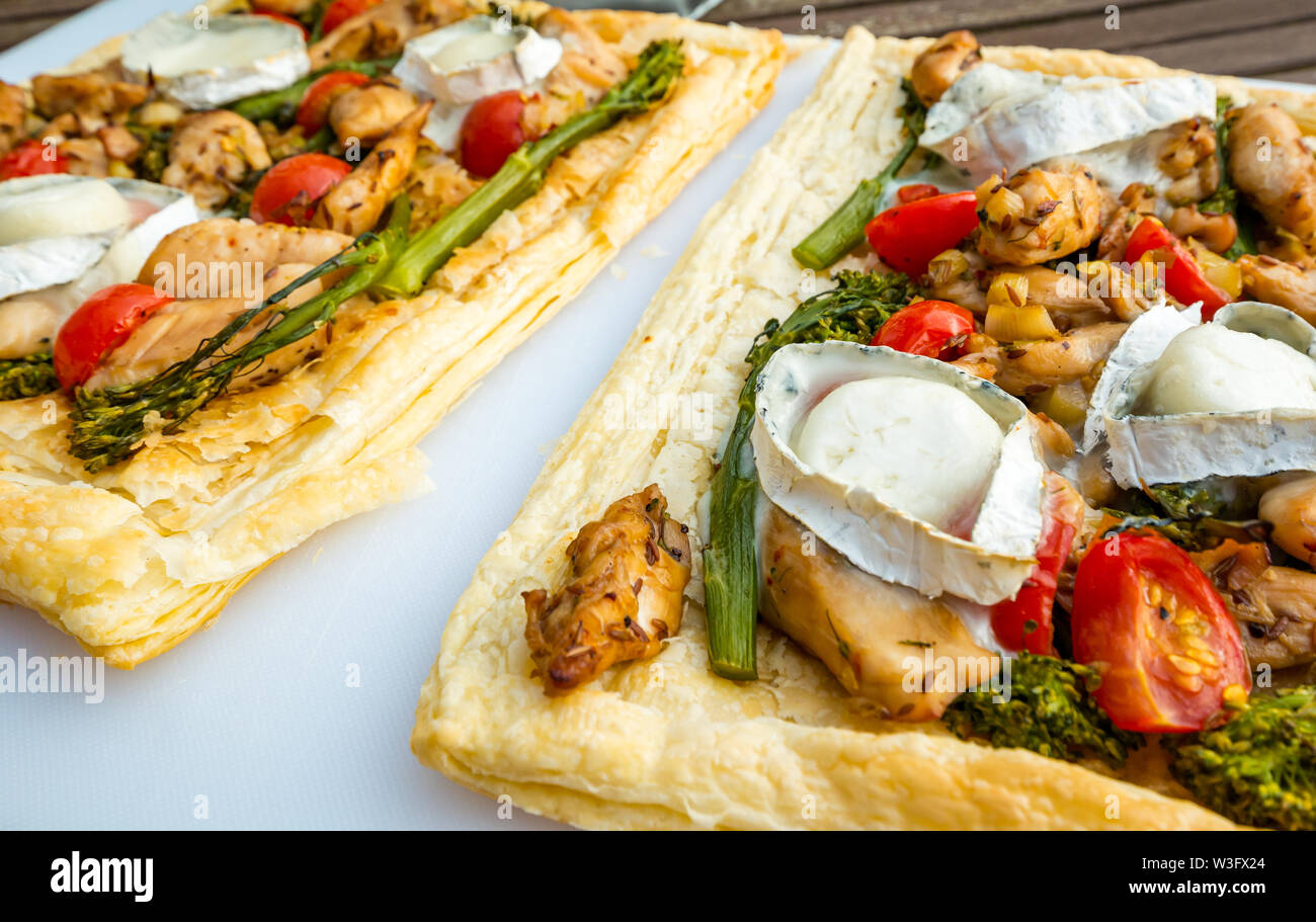 Estate cibo: pasto servito all'aperto con formaggio di capra, broccoli, pomodori e pollo su pasta sfoglia fette Foto Stock