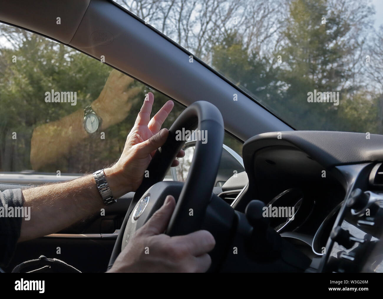 Driver è lampeggia in segno di vittoria mentre la primavera paesaggio è lampeggiante nella finestra auto. Foto Stock