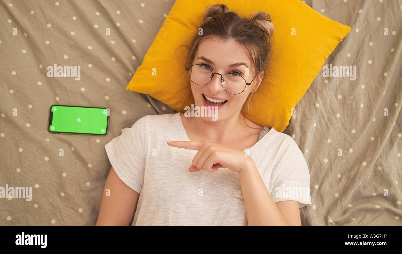 In prossimità di una ragazza rilassato utilizzando uno smart phone mentre giaceva sul letto di casa. Foto Stock