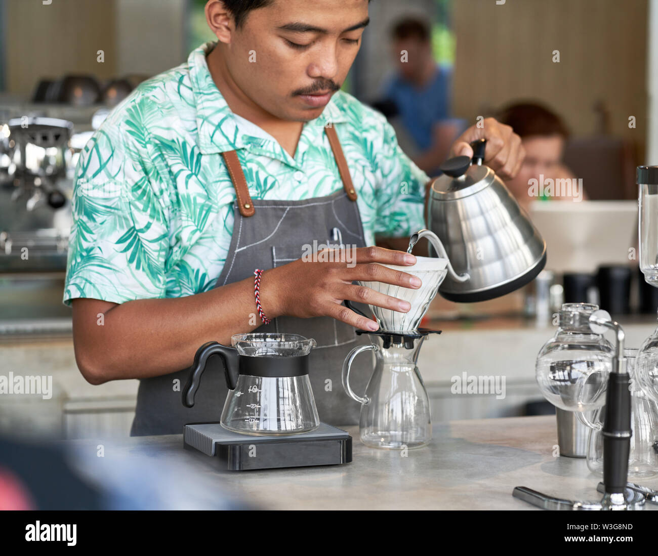 Schietto stile di vita colpo di sorridente indonesiano etnica barista e proprietario di piccola impresa la preparazione di organic fair-trade caffè nella luminosa trendy coffee shop Foto Stock