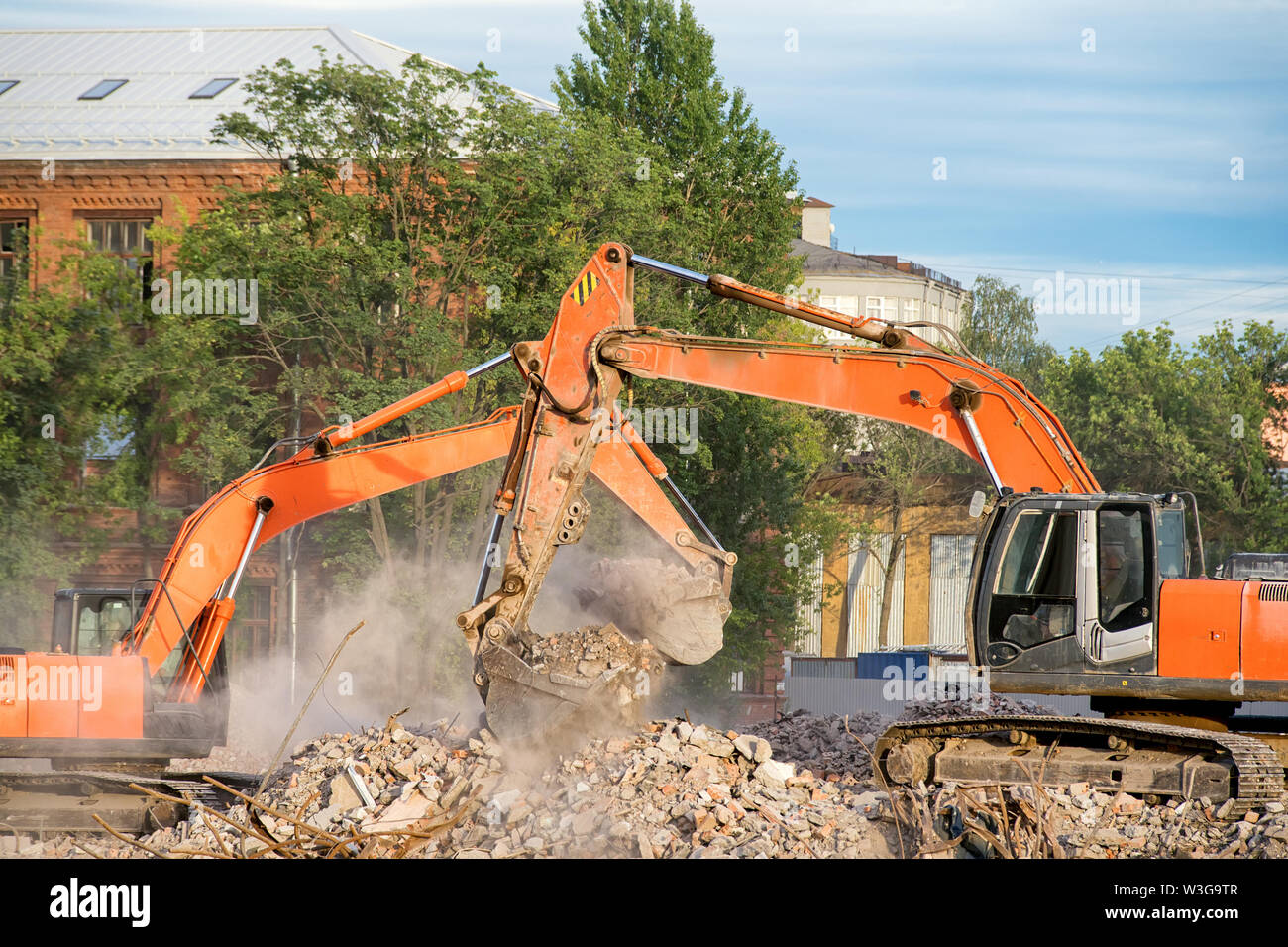 Due escavatori arancione lavorando sui resti di un edificio demolito. La pulizia dei detriti di demolizione di costruzione e di cancellazione del sito immagine a tema Foto Stock