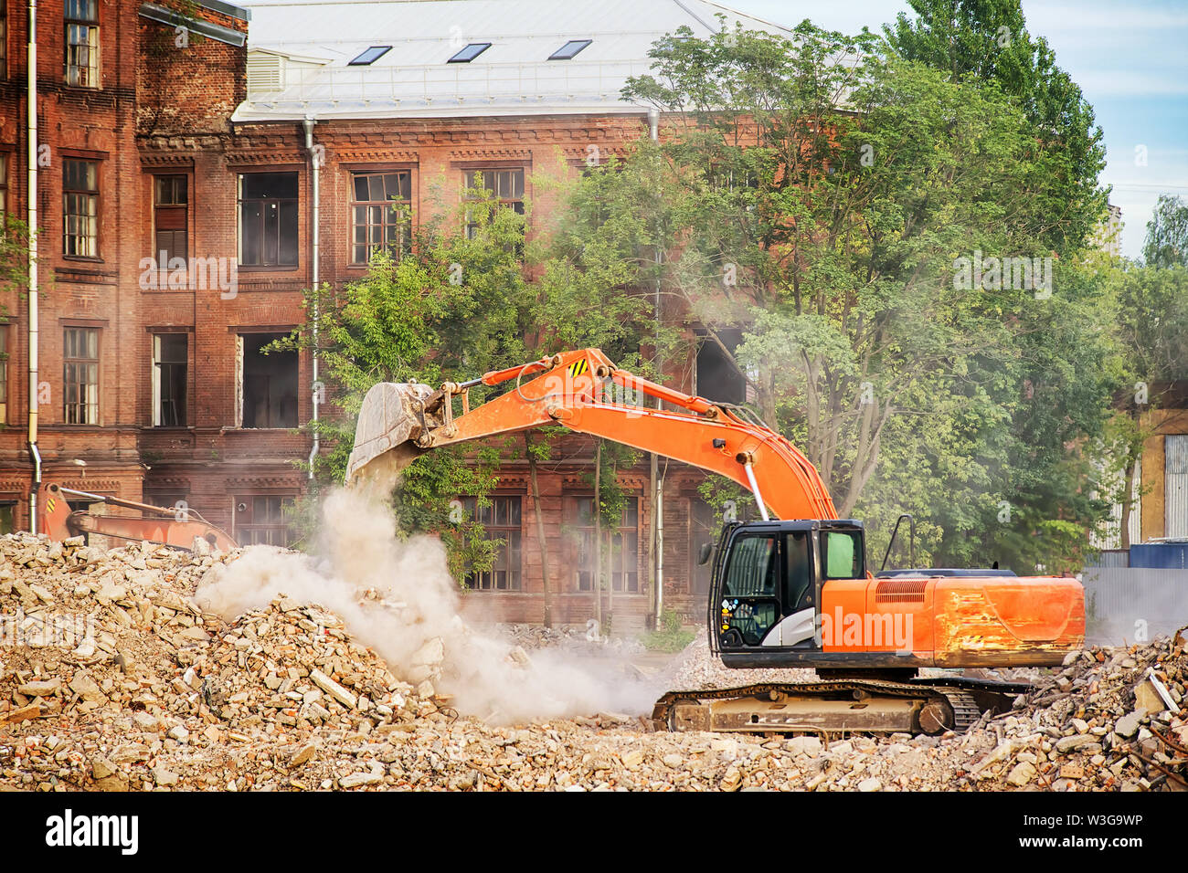 Escavatore arancione lavorando sulle rovine di un edificio demolito. La pulizia dei detriti di demolizione di costruzione e di cancellazione del sito immagine a tema Foto Stock