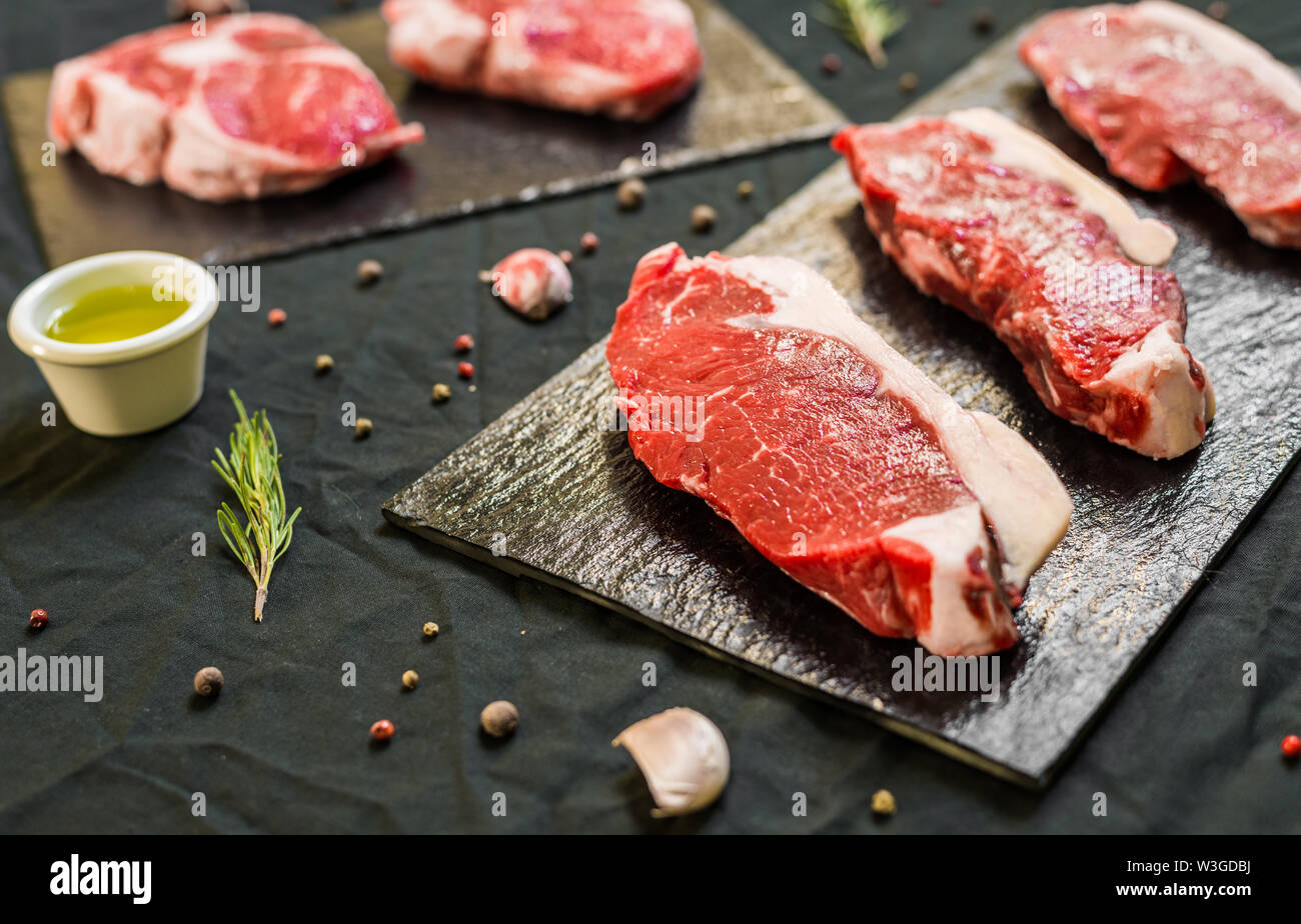 Carni bovine Vacca bistecche di carne con le spezie e le erbe su sfondo nero Foto Stock