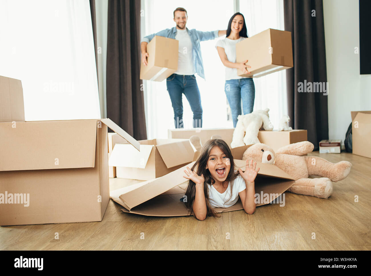 Bambina giocando con le scatole di cartone. La figlia in movimento nella casa nuova con i suoi genitori Foto Stock