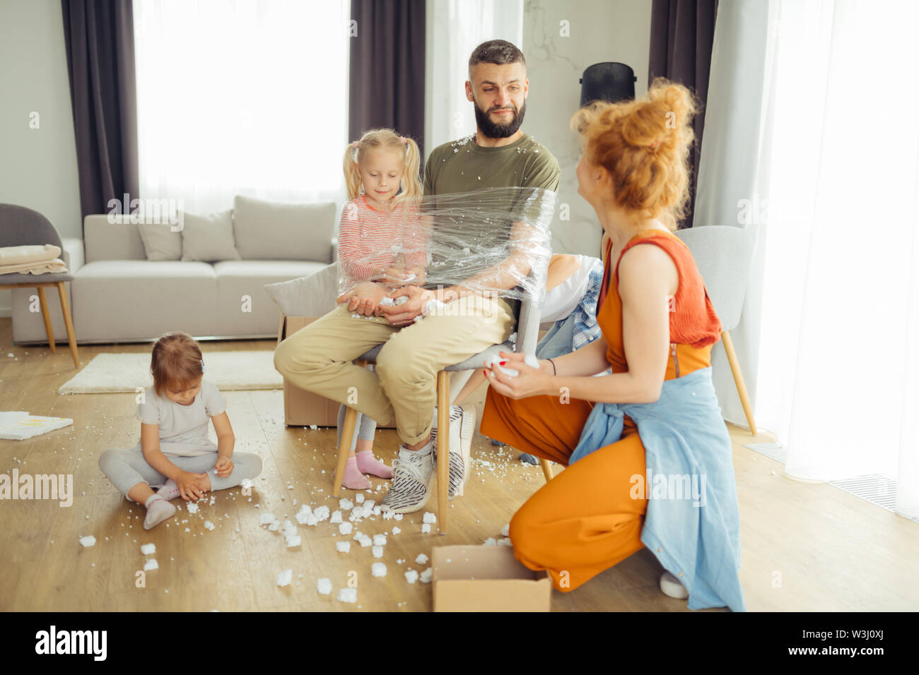 Giochi divertenti. Nizza uomo barbuto essendo legato alla sedia mentre gioca con i suoi figli Foto Stock