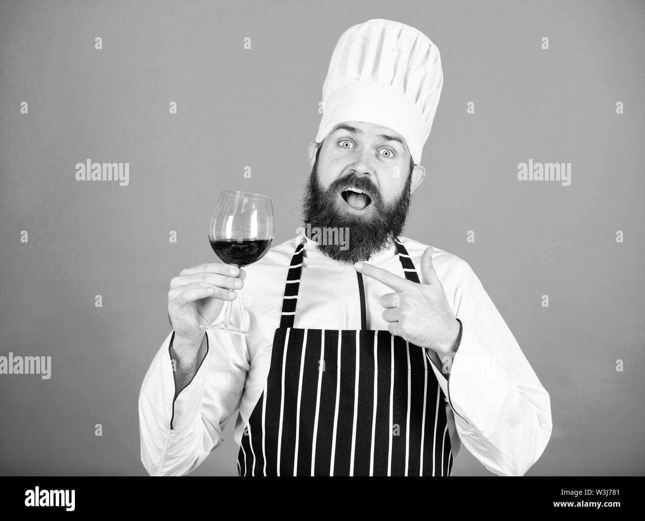 Sommelier al lavoro. La bevanda alcolica. Vino rosso in vetro. Felice l'uomo barbuto. Chef professionale in cook uniforme. Questo vino è semplicemente perfetto. Fiducioso sommelier maschio esaminando il vetro con il vino. Foto Stock