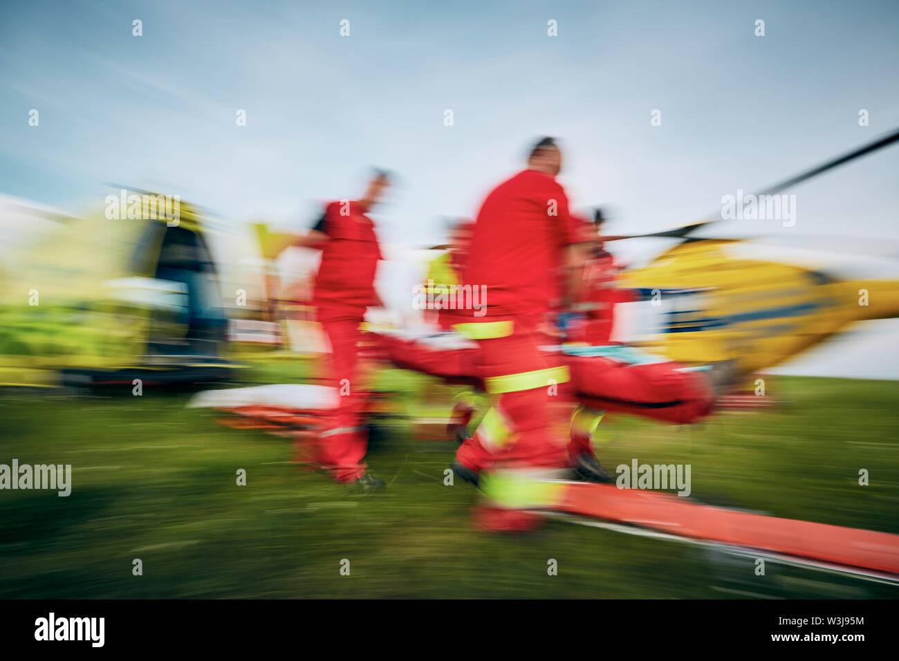 Team di servizio di emergenza medica che porta paziente in movimento sfocate contro ambulanza ed elicottero. Foto Stock