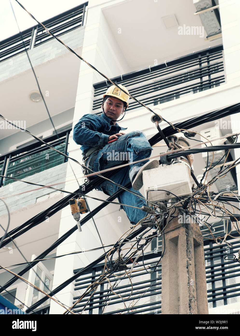 Elettricità vietnamita lavoratore salita elevato su elettrico post per la riparazione della rete elettrica, uomo opera in servizio non sicuri a mezzogiorno, Vietnam, città di Ho Chi Minh Foto Stock