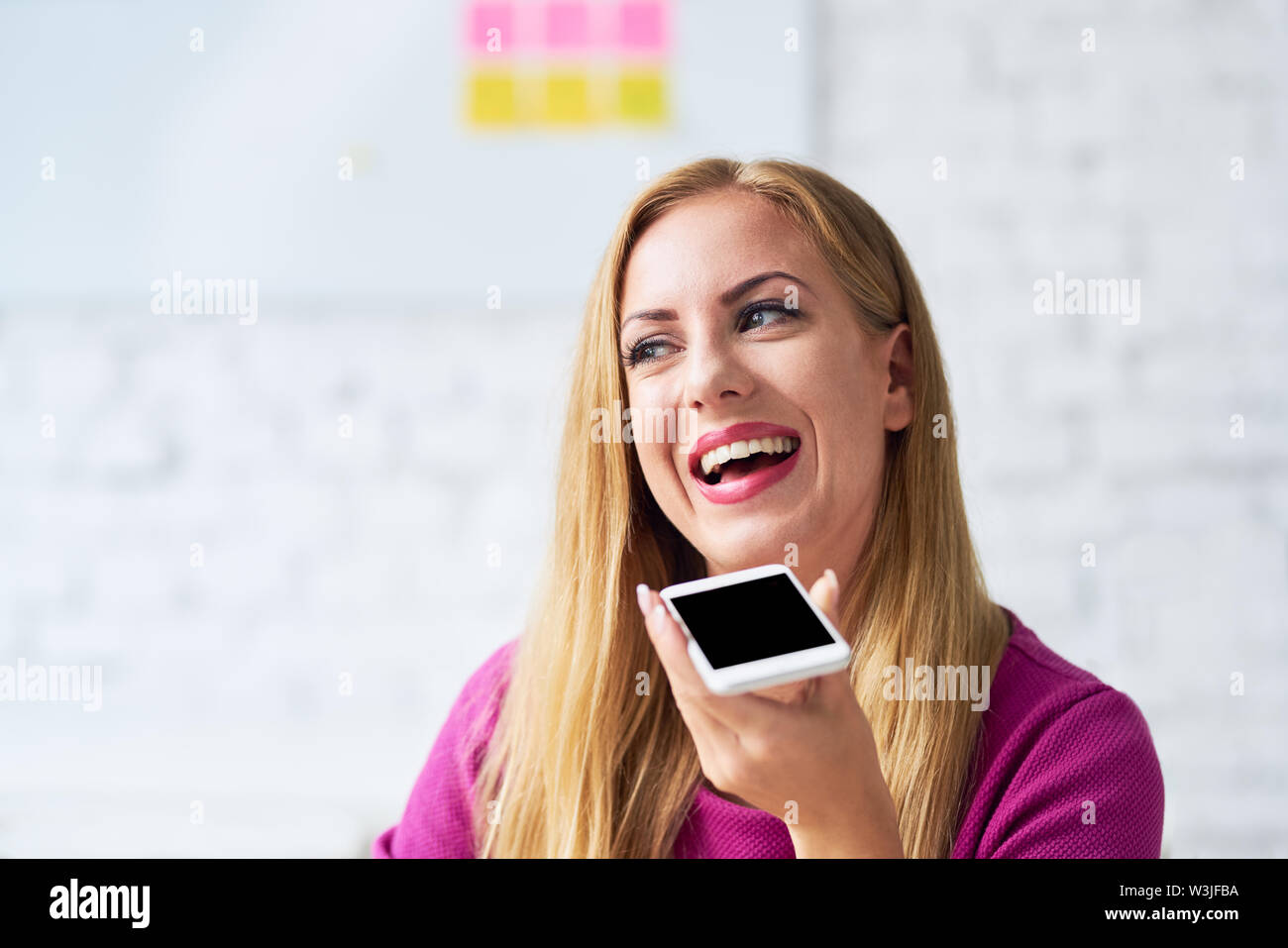 Donna felice di parlare al telefono in ufficio utilizza lo smartphone altoparlante in ufficio Foto Stock