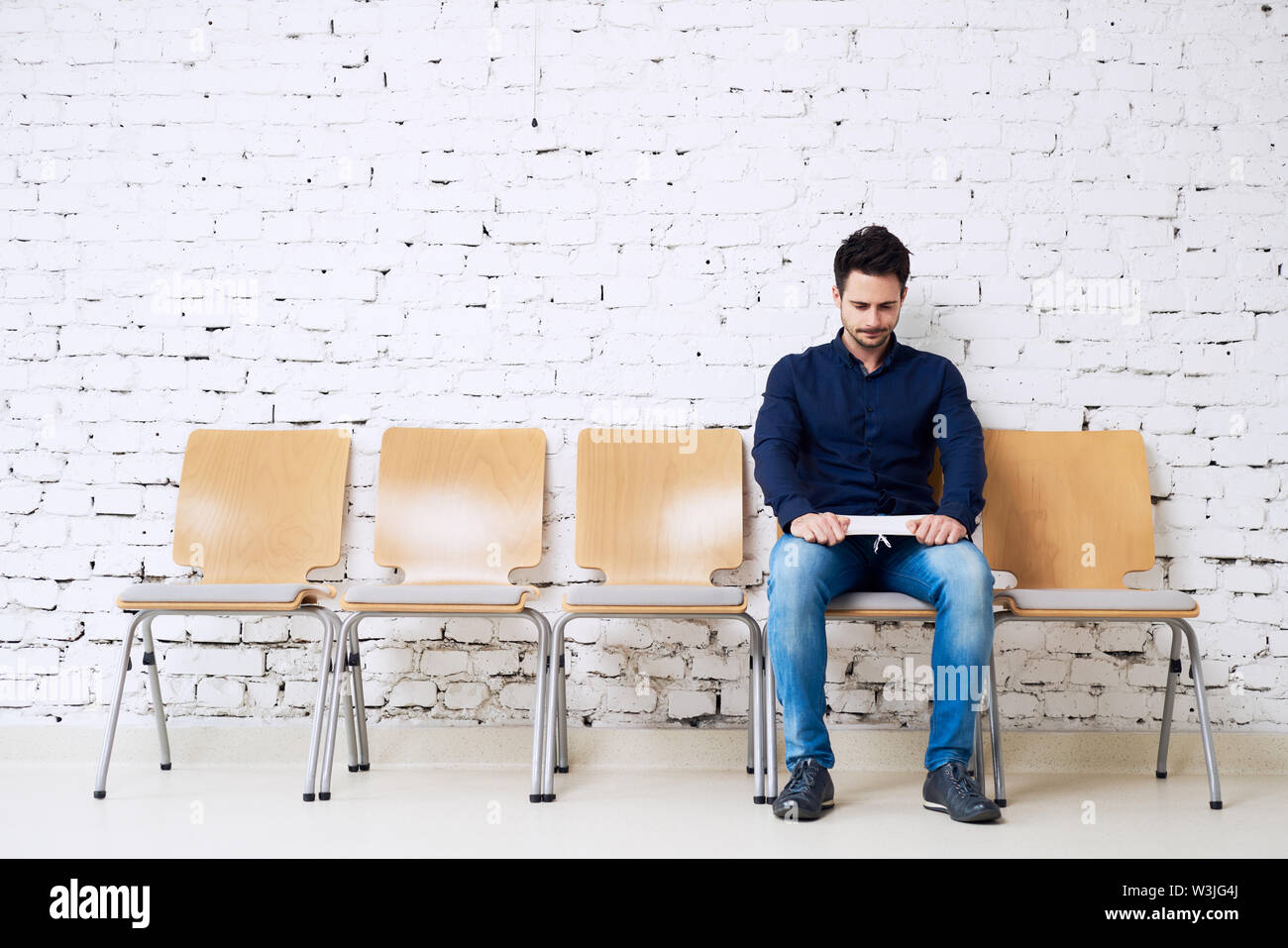 Sottolineato giovane uomo seduto su una sedia in attesa per il colloquio di lavoro nella società moderna Foto Stock